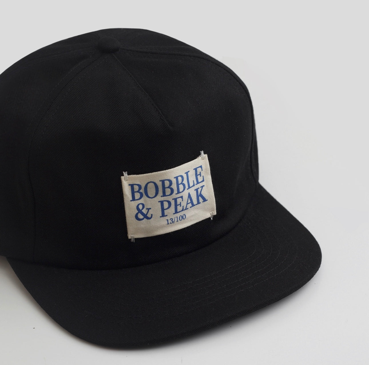 Classic Bobble and Peak black baseball cap with white logo label front view