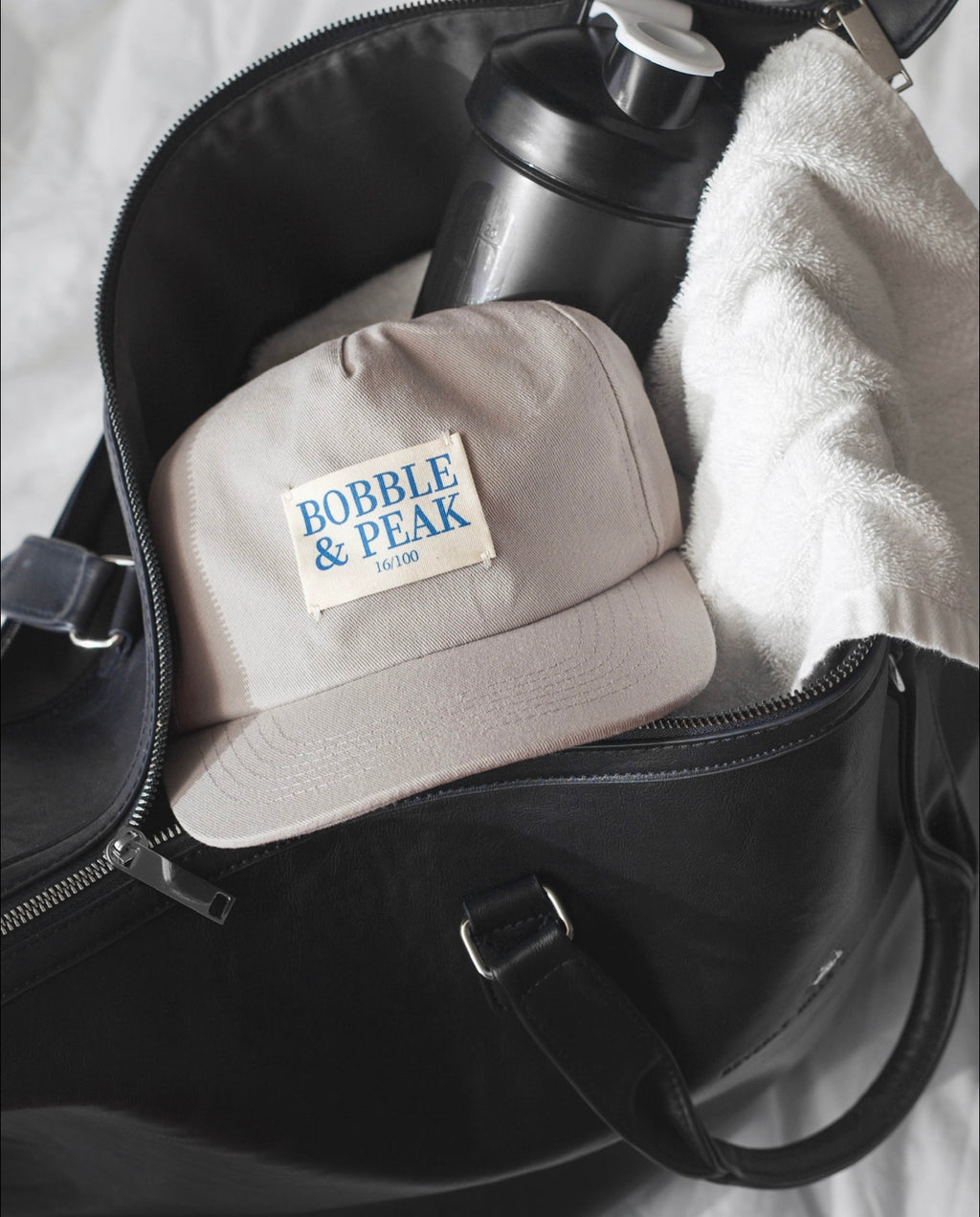 Grey cap with 'Bobble & Peak' logo inside a black bag.